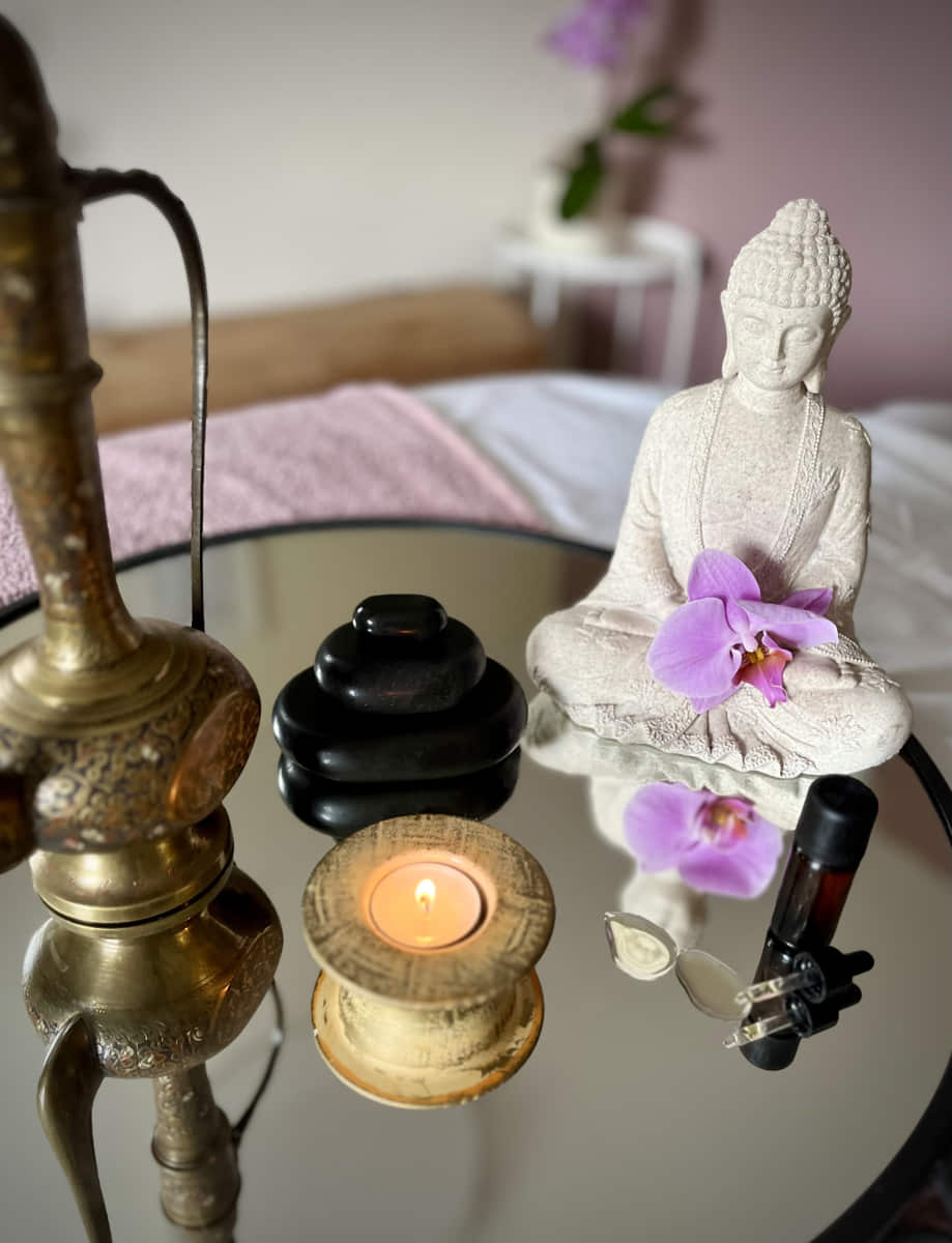 hohe metallene fein ziselierte Kanne, gestapelte Hotstones, Teelicht brennt in steinernem Teelichthalter, steinerner Buddha mit Blüte
